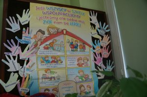 zdjęcie przewdstawiające gazetkę szkolną na której napisane są zasady dobrego zachowania i rączki papierowe na których napisane sąimiona dzieci