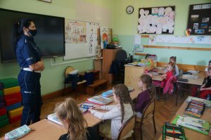 zdjęcie zrobione w sali lekcyjnej widać boekim stojącą na środku sali policjantkę która rozmawia z dziecmi dzieci siedzą w ławkach
