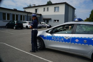 policjantka stoi obok zaparkowanego radiowozu w tle plac  przy szkole