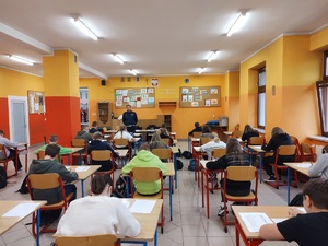 zdjęcie kolorowe sala lekcyjna uczniowie siedzą tyłem przy stolikach i rozwiązują testy