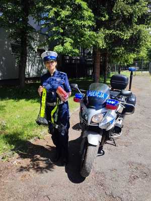 policjantka trzyma odblaskową kamizelkę oraz inne przedmioty dla motocyklistów stoi obok policyjnego motocykla