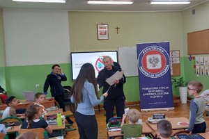 zdjęcie kolorowe zrobione w sali policjantka wręcza dzieciom nagrody za udział w konkursie