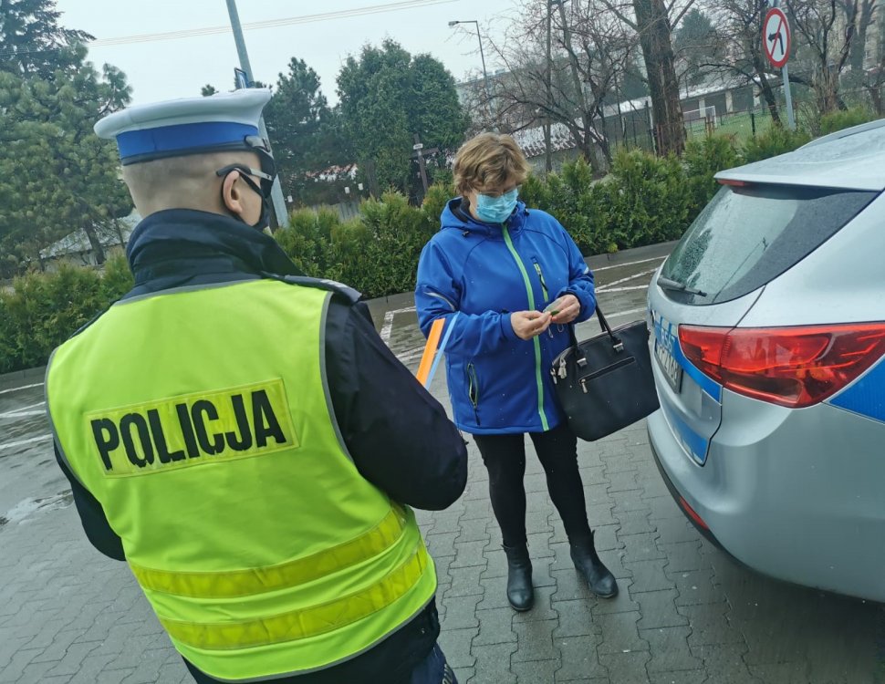 policjant stoi tyłem obok stoi kobieta policjant dajej jej mandat obok samochód i radiowóz w tle bloki