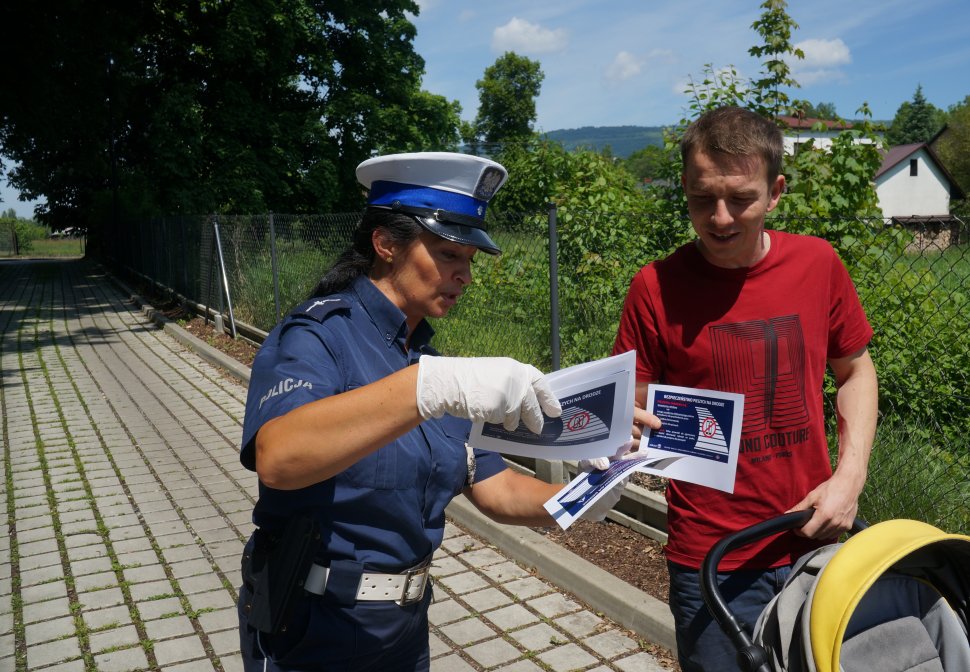 policjantka wręcza męzczyźnie ulotkę stoją obok siebie są przodem do obiektywu