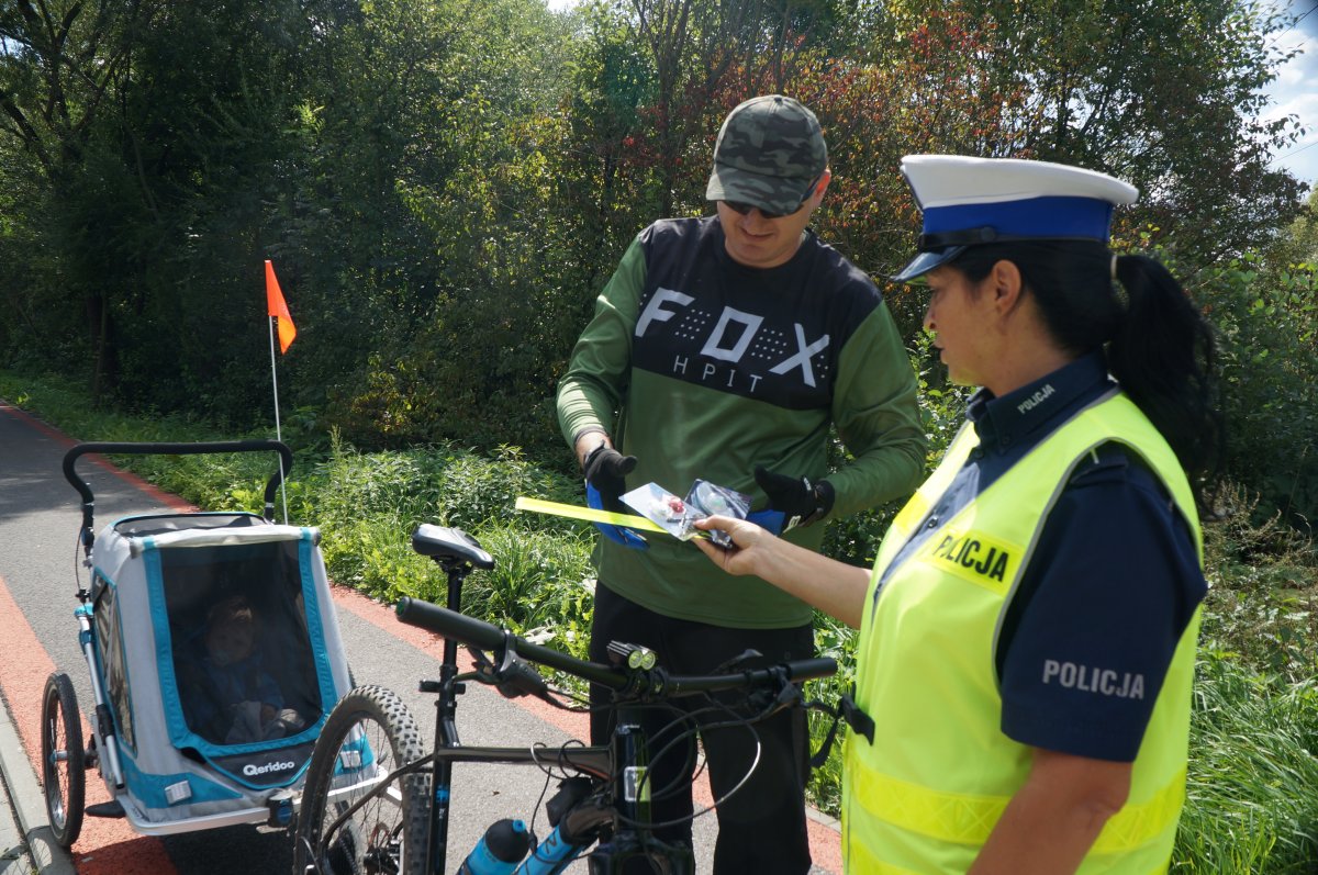 obok siebie stoi policjntka i rowerzysta policjantka wręcza mu elementy odblaskowe