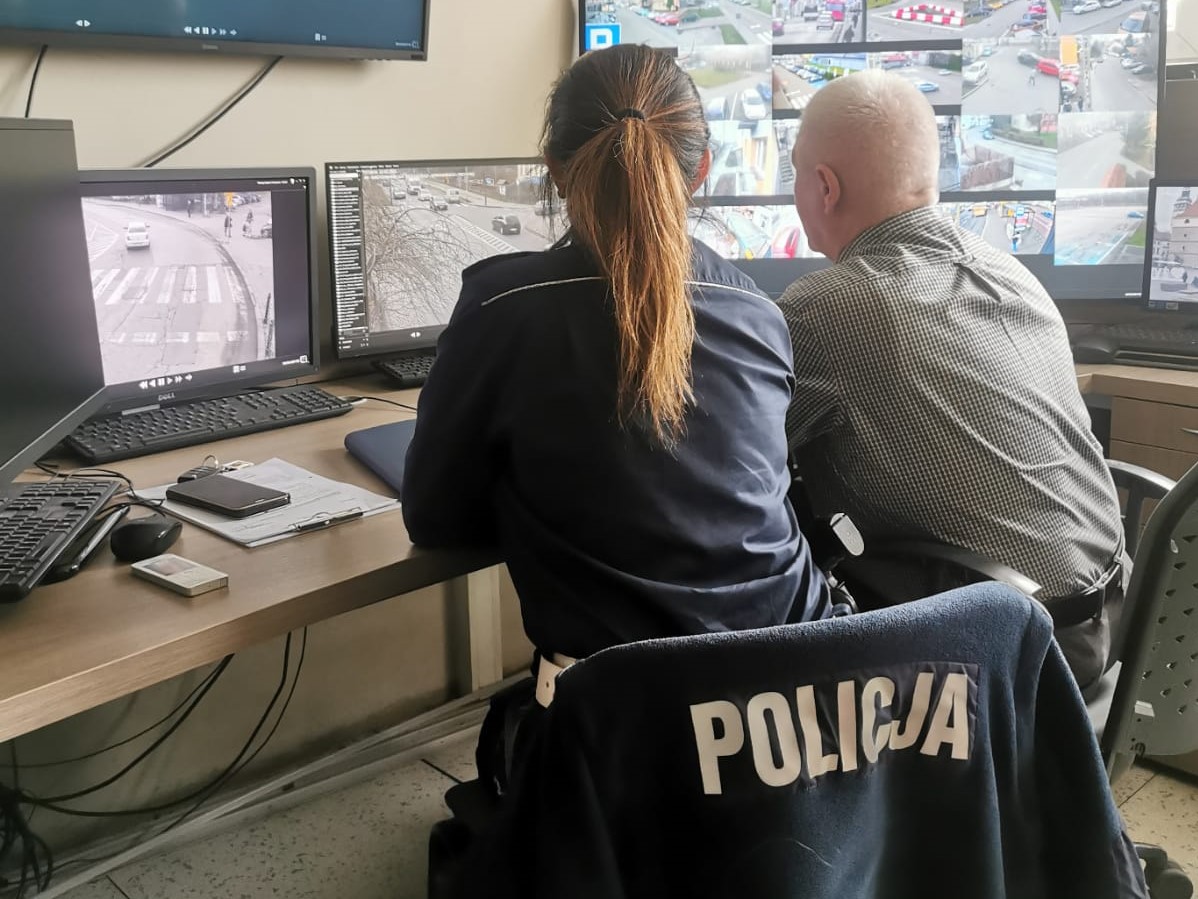 zdjecie zrobione w pomieszczeniu tyłem na krzesłach siedzi policjantka oraz strażnik miejski przed nimi monitory z zapisem z kamer