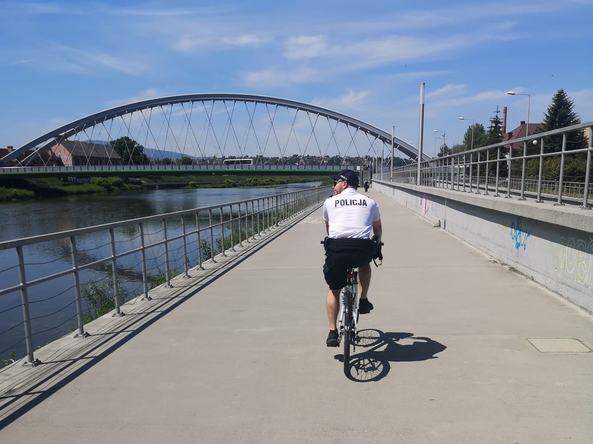 ścieżka rowerowa obok rzeki po której jedzie policjant na rowerze zdjecie kolorowe