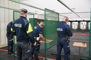 trzech policjantów ładuje magazynki, w tle instruktor