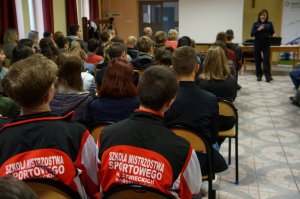 uczniowie siedzący tyłem oraz policjantka w czasie prelekcji