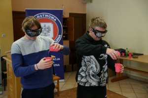dwóch uczniów z alkogooglami wykonuje zadanie wlewania wody do kubka