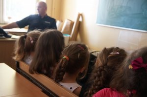 w ławce siedzi pięć dziewczynek tyłem w tle policjant