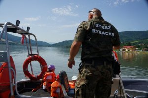 funkcjonariusz straży rybackiej pomaga dzieciom wejść do motorówki