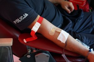 fragment koszuli z napisem policja oraz ręki z igłą w czasie poboru krwi