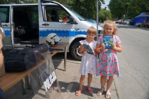 dziewczynki na tle radiowozu trzymają książeczki edukacyjne