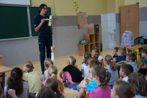 policjantka trzyma odblaski dzieci siedzą tyłem