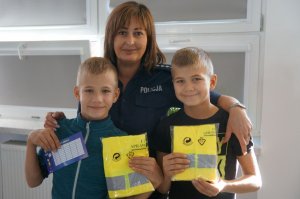 policjantka z uczniami którzy trzymają kamizelki odblaskowe