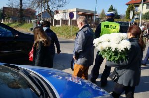 fragment radiowozu, policjant oraz ludzie idący na cmentarz