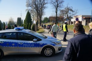 radiowóz, policjant oraz ludzie idący na cmentarz