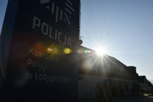 pylon z napisem komisariat policji w Łodygowicach, w tle komisariat oraz ludzie