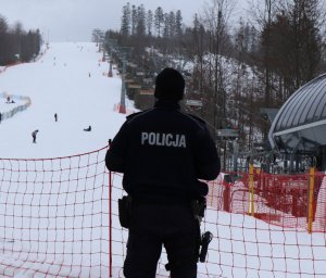 policjant stoi tyłem w tle stok i wyciąg narciarski