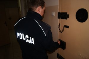 policjant tyłem, widoczny napis policja, otwiera pomieszczenie dla zatrzymanych