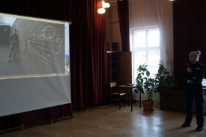 na ekranie widoczny spot profilaktyczny policjantka stoi z boku z mikrofonem
