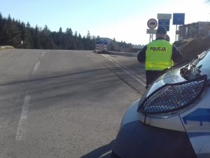 policjant stoi tyłem widać fragment radiowozu w tle krajobraz