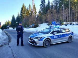 policjant obok radiowozu w tle domy