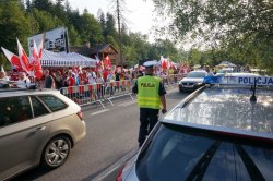 fragment radiowozu obok stoi policjant w tle ulica z lewej strony zdjęcia tłum kibiców