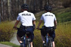 policjanci jadą na rowerach, na białych koszulach na plecach napis policja,