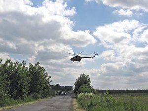 lecący śmigłowiec, w tle las oraz radiowóz