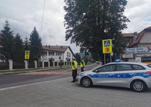 policjanci stoją przy radiowozie w rejonie przejścia DLA PIESZYCH PRZY SZKOLE