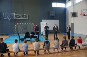 na środku sali stoją policjanci burmistrz oraz dyrekcja dzieci siedzą na ławce