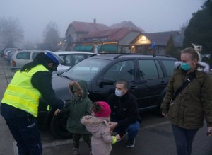 policjantka wręcza odblask dziecku z boku stoją inne osoby