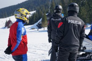 dwóch policjantów stoi tyłem widoczny napis policja obok stoi ratoenik górskiego ochotniczego pogotowia ratunkowego