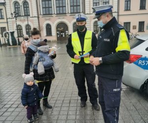 policjanci stoją obok siebie w tle radiowóz obok policjantów kobieta z dwójką dzieci trzyma odblaski