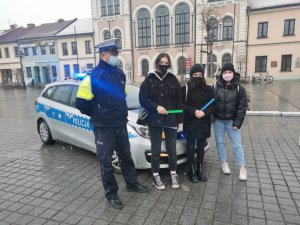 policjant stoi obok radiowozu, obok niego stoją trzy kobiety z odblaskami