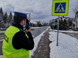 policjant stoi tyłem trzma urządzenie do pomiaru prędkości w tle ulica