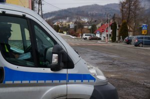 zdjęcie kolorowe widoczny fragment radiowozu w środku siedzi policjant w tle widoczne skrzyżowanie