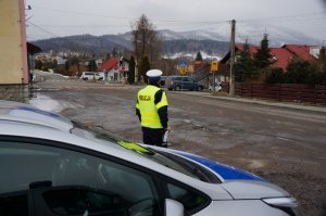 zdjęcie kolorowe fragment radiowozu obok stoi policjant w tle widoczne skrzyżowanie