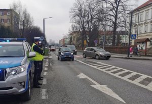 dwóch policjantów stoi obok radiowozu obok ulica i samochody widoczne przejście dla pieszych