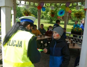 policjantka wręcza odblask dziecku, wtle siedzą inne dzieci zdjęcie kolorowe