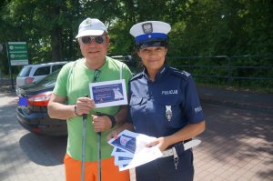 policjantka i pieszy stoją obok siebie trzymają ulotki w tle samochody zaparkowane na parkingu