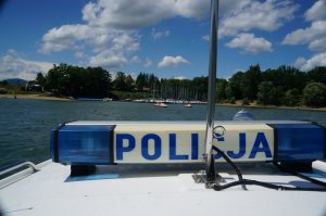 fragm,ent policyjnej motorówki widoczny napis policji w tle jezioro i plaża