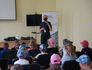 dzieci siedzą tyłem w tle policjantka w czasie prelekcji prelekcja odbywa się w slai