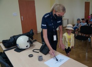 policjantka w czasie pobierania odcisków palcy obok stoi dziewczynka w tle inne dzieci