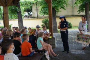 policjantka w czasie prelekcji obok stoi kobieta która trzyma plansze z zakresu bezpieczeństwa w ruchu drogowym obok siedzą dziecfi