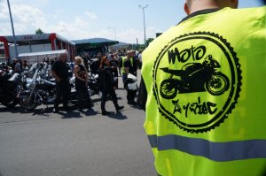 na pierwszym planie fragment mężczyzny stoi tyłem na założoną odblaskową kamizelkę z napisem moto Żywiec w tle motocykliści