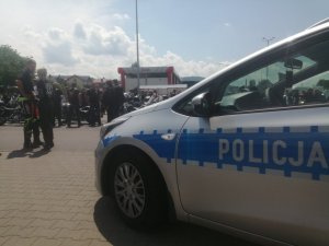 fragment radiowozu widoczny napis policja w tle inne zaparkowane samochody i motocykle