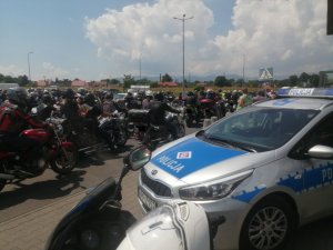 fragment policyjnego radiowozu i policyjnego motocykle w tle inni motocykliści na motorach